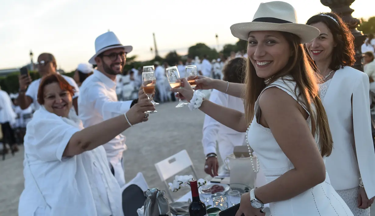 Peserta dalam balutan serba putih  bersulang sampanye saat Dinner en Blanc atau "makan malam putih" di Tuileries Gardens, Paris, Kamis (6/6/2019). Peserta acara ini harus diundang oleh mereka yang sudah terdaftar di situsnya atau mengenal salah satu penyelenggara Diner en Blanc (Lucas BARIOULET/AFP)