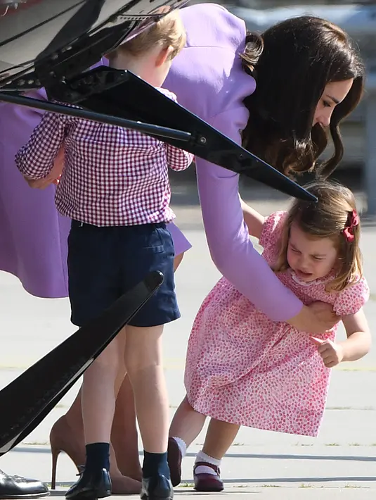 Kate Middleton berusaha menggendong anaknya, Putri Charlotte, yang merajuk dalam kunjungan mereka ke Pabrik Airbus di Hamburg, 21 Juli 2017. Putri Charlotte mendadak merajuk dan enggan naik helikopter di pabrik pesawat terbang itu. (Patrik STOLLARZ / AFP)