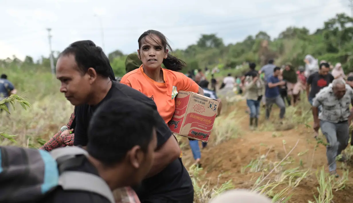 Pemerintah memastikan distribusi bantuan menjangkau seluruh wilayah, termasuk wilayah yang masih terisolir. Tampak dalam foto, para penyintas banjir membawa barang-barang bantuan yang didistribusikan oleh helikopter TNI AU di Aceh Tengah, Sabtu 6 Desember 2025. (AP Photo/Reza Saifullah)