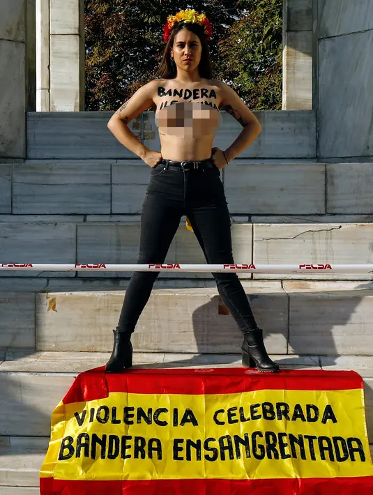 Aktivis perempuan Femen berdiri sambil menunjukkan tulisan "Illegitimate flag" di dadanya dan bendera Spanyol 'Celebrated violence bloody flag' saat unjuk rasa di monumen Konstitusi Spanyol 1978 di Madrid, (11/10). (AFP Photo/Oscar Del Pozo)