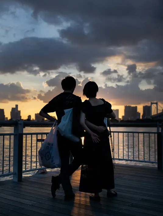 Pasangan menikmati matahari terbenam di Odaiba, Tokyo, (29/7). Odaiba adalah sebuah pulau buatan di Teluk Tokyo, Jepang yang dihubungkan dengan pusat kota Tokyo dengan Jembatan Rainbow. (AFP Photo/Martin Bureau)