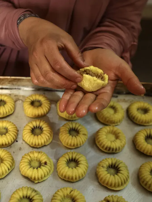 <p>Perempuan Palestina membuat kue tradisional berisi kurma dan kacang-kacangan dalam persiapan untuk liburan Idul Fitri, di kota Hebron, Tepi Barat, pada 28 April 2022. Orang-orang di Palestina mempunyai tradisi lebaran yang unik dan khas yaitu dengan membuat kue kering dengan aneka bentuk dan rasa. (HAZEM BADER / AFP)</p>