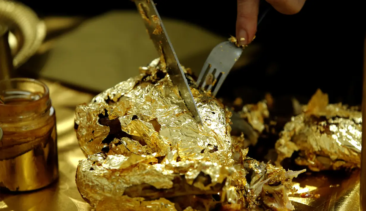 Seniman Prancis, Frederique Lecerf membungkus ayam dengan lembaran emas tipis 24 karat dalam acara makan malam di Paris, 28 Maret 2019. Lembaran tipis emas menyelimuti makanan sederhana seperti ayam, telur rebus, dan kue-kue berlapis emas untuk pencuci mulut. (REUTERS/Philippe Wojazer)