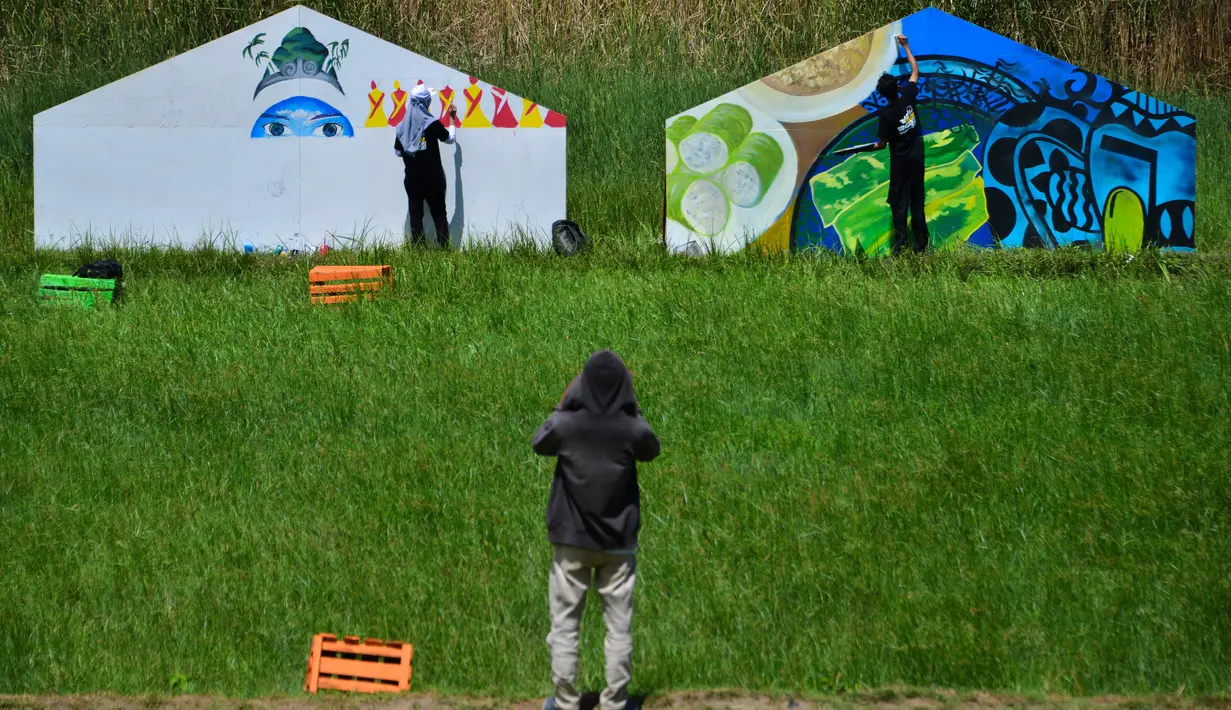 Seorang pria melihat seniman lokal melukis mural di tengah sawah selama The Art of Color Sensation 2019 di desa wisata Gampong Nusa, Lhoknga, Aceh, Minggu (16/6/2019). Kegiatan yang mengangkat kearifan lokal lewat seni mural ini menjadi media promosi bagi Gampong Nusa. (CHAIDEER MAHYUDDIN/AFP)