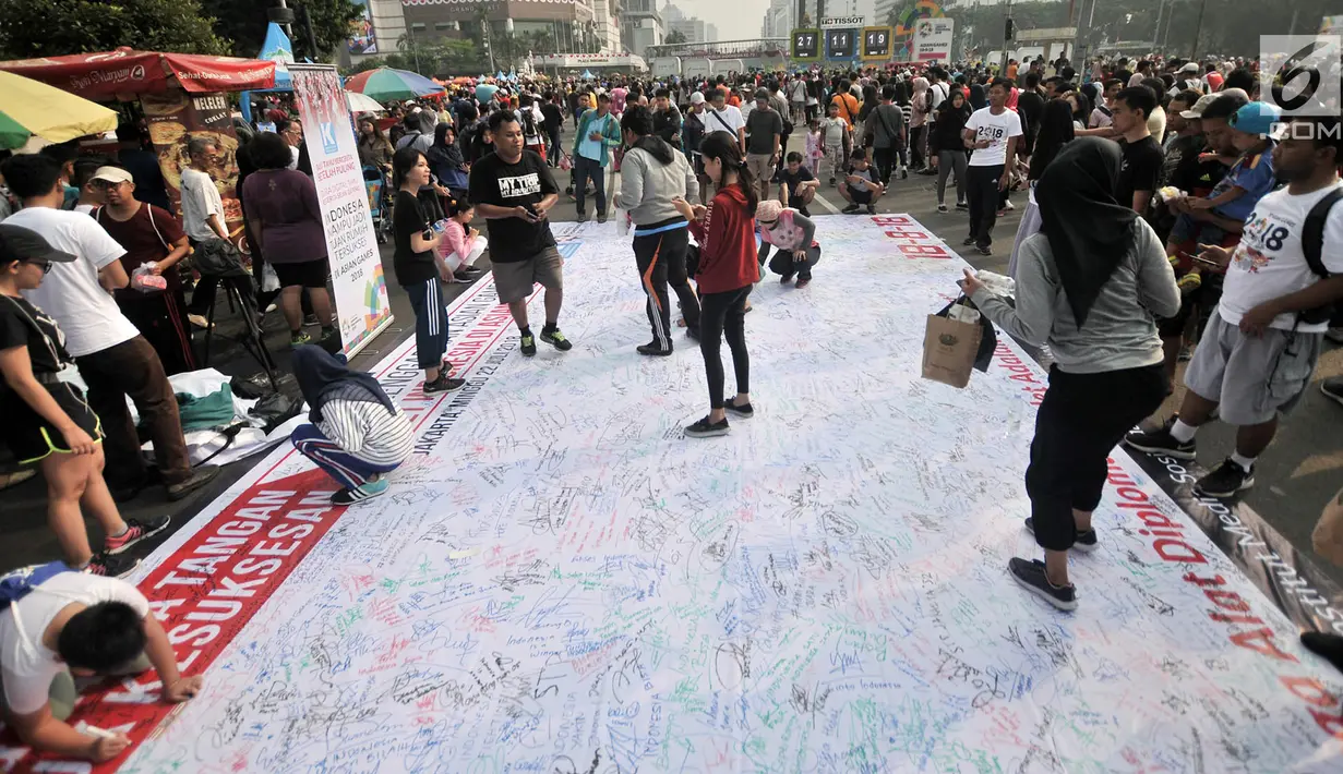 Pengunjung membubuhkan tanda tangan di atas spanduk raksasa saat car free day (CFD) di Bundaran HI, Jakarta, Minggu (22/7). Doa dan pengumpulan tanda tangan ini diinisiasi Komunikonten untuk mendukung atlet Asian Games 2018. (Merdeka.com/Iqbal Nugroho)