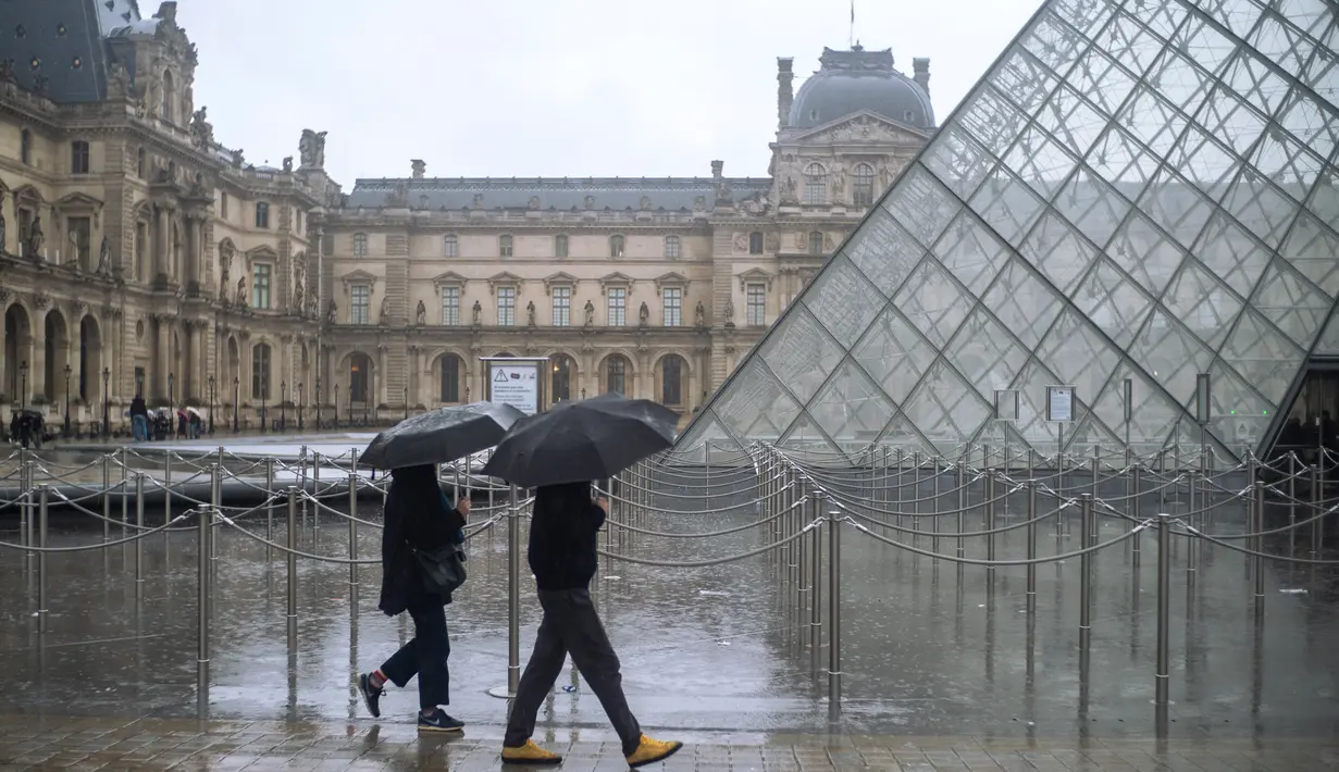 Orang-orang berjalan melintasi museum Louvre di Paris pada Minggu (1/3/2020). Louvre, museum yang paling banyak dikunjungi di dunia, ditutup sementara untuk pengunjung setelah para staf menolak bekerja di tengah kekhawatiran terjangkit virus corona tipe baru, Covid-19. (AP/Rafael Yaghobzadeh)