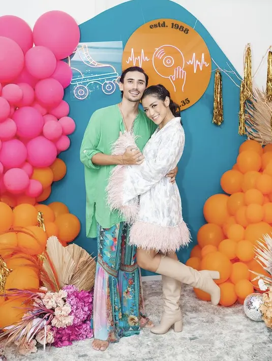 Selain itu, Jessica mengenakan dress lengan terompet warna putih bermotif. Dengan aksesn bulu-bulu di bagian lengan dan bawah dress. Sedangkan sang suami, tampil mengenakan kemeja panjang hijau dipadukan celana panjang loose bemotif