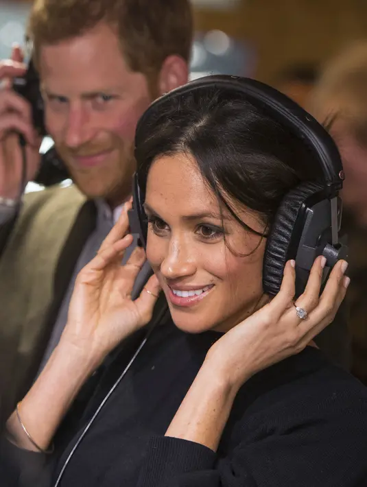 Meghan Markle (depan) dan Pangeran Harry (belakang) menjajal headset saat kunjungan ke stasiun radio Reprezent 107,3 FM di Brixton, London, Selasa, (9/1). Pasangan ini ingin melangsungkan pernikahan di Frogmore House. (AP Photo/Dominic Lipinski, Pool)