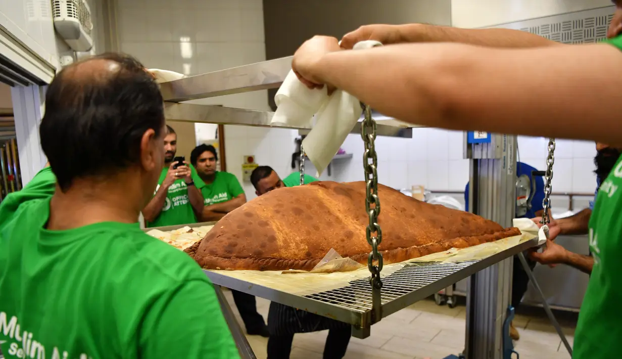 Koki dan relawan Muslim Aid menimbang berat makanan ringan berbentuk segitiga, samosa raksasa, di Masjid London Timur, Inggris, Selasa (22/8). Total pengerjaan samosa raksasa ini membutuhkan waktu mencapai 15 jam untuk menyelesaikan. (BEN STANSALL/AFP)