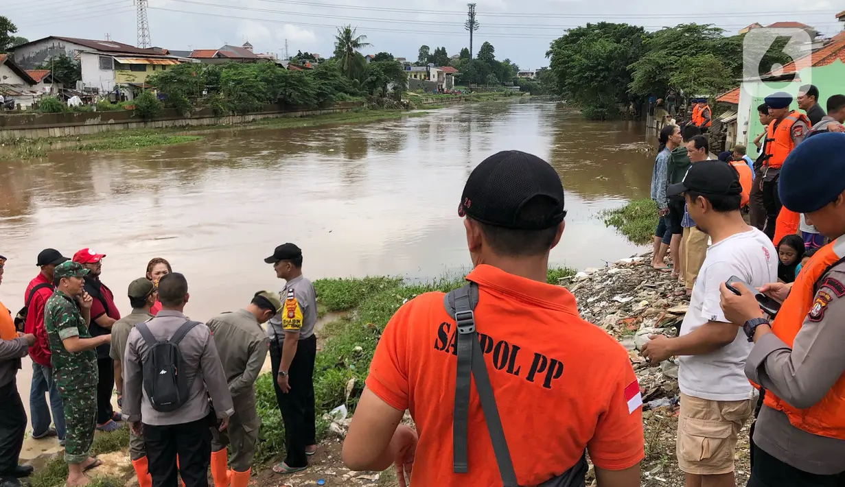 Warga bersama personel kepolisian, Satpol PP, dan TNI berkumpul di bantaran Sungai Ciliwung, Jakarta, Selasa (25/2/2020). Adanya warga yang hanyut saat berenang di tengah luapan Sungai Ciliwung mengundang perhatian warga dan petugas yang mencari keberadannya. (Liputan6.com/Immanuel Antonius)