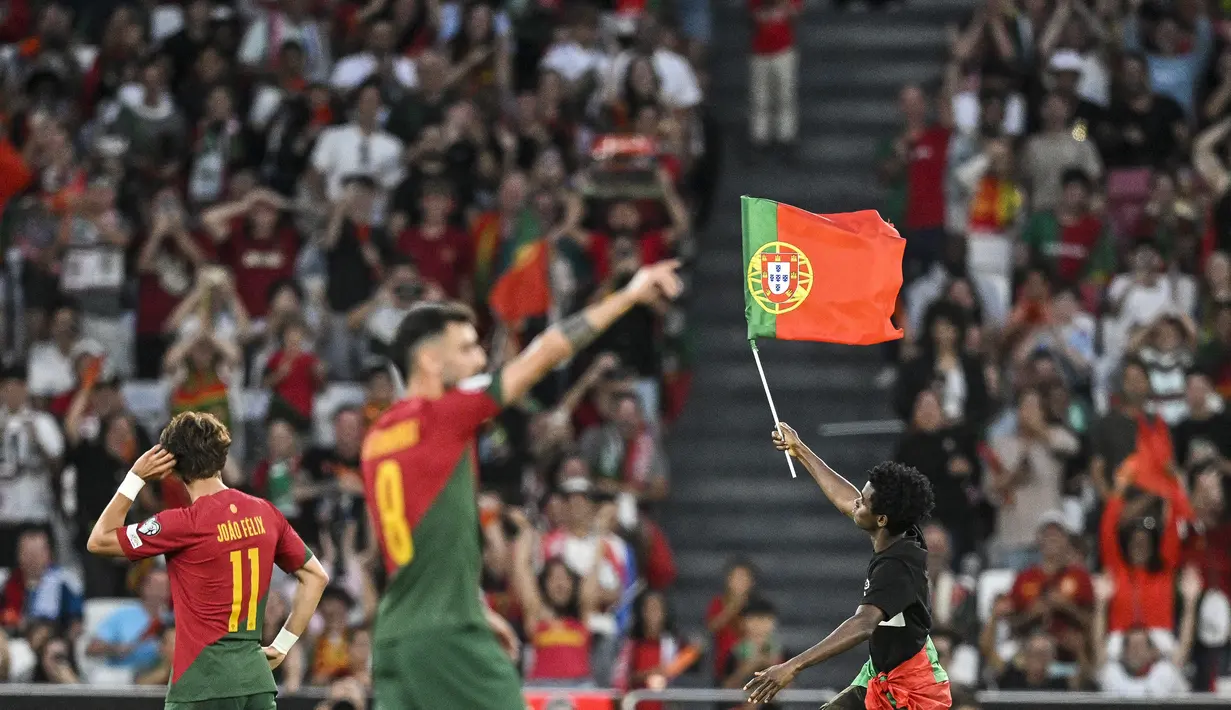 Seorang penyusup lapangan berlari sambil mengibarkan bendera Portugal di tengah laga Grup J Kualifikasi Euro 2024 antara Timnas Portugal menghadapi Bosnia Herzegovina di Luz Stadum, Lisbon, Portugal, Minggu (18/6/2023) dini hari WIB. (AFP/Patricia De Melo Moreira)