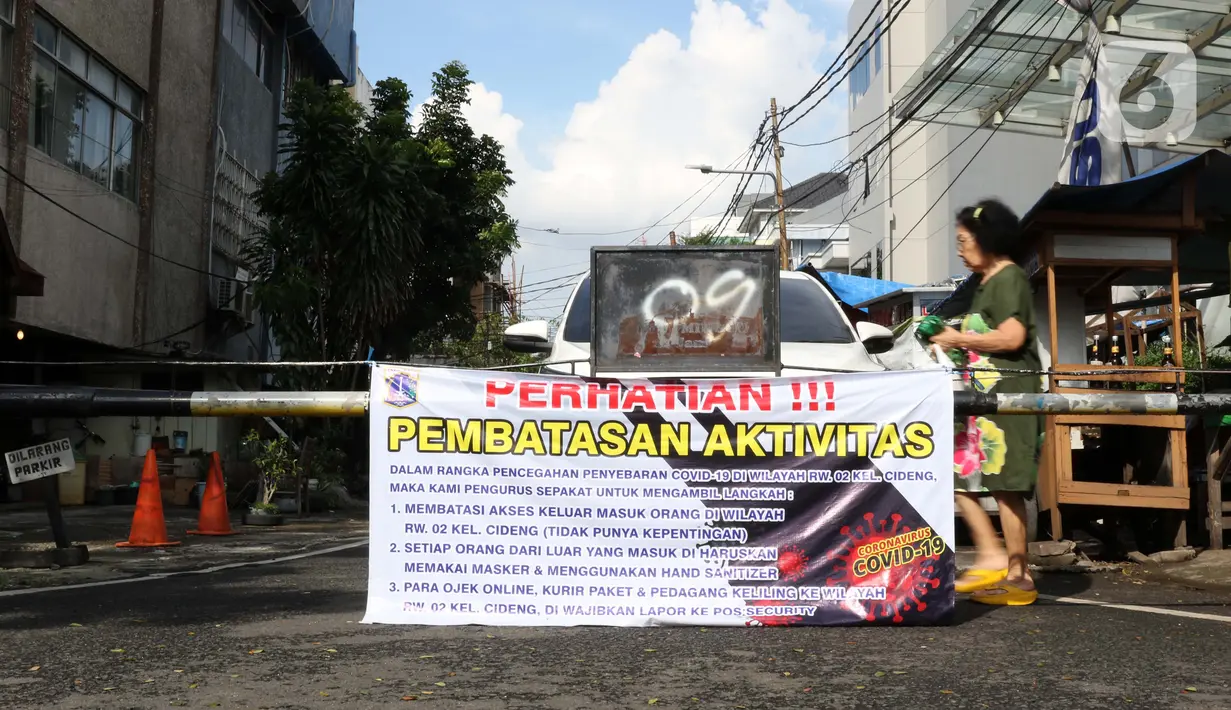 Warga melintasi portal yang terpasang spanduk pembatasan aktivitas di pintu masuk perumahan, Cideng, Jakarta, Kamis (2/4/2020). Pemerintah menetapkan Pembatasan Sosial Berskala Besar dengan membatasi kegiatan tertentu di wilayah yang diduga terinfeksi COVID-19. (Liputan6.com/Helmi Fithriansyah)
