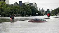 Warga melintas dekat sebuah mobil yang terendam banjir setelah Badai Harvey menghantam kota Houston, Texas, Minggu (27/8). Banjir bandang yang dibawa Badai Harvey telah membuat Houston, kota terbesar keempat di AS, semakin terisolasi (AP/David J. Phillip)
