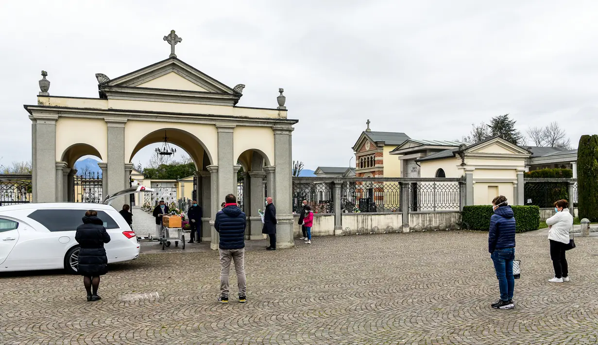 Kerabat seorang warga yang sudah meninggal menjaga jarak aman saat berkumpul dalam upacara pemakaman selama masa lockdown untuk menghentikan penyebaran pandemi virus corona COVID-19 di luar kuburan kecil Bolgare, Lombardy, Italia, Senin (23/3/2020). (Piero CRUCIATTI / AFP)