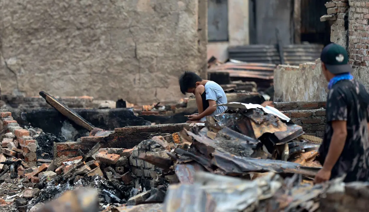 Seorang anak melihat telepon pintarnya di lokasi bekas kebakaran di permukiman padat penduduk di Jalan Kemayoran Gempol belakang Pasar Jiung, Kelurahan Kebon Kosong, Kecamatan Kemayoran, Jakarta Pusat, Selasa (2/6/2026). (Kapanlagi.com/Budy Santoso)