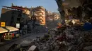 Seorang pria membawa ember saat berjalan di antara bangunan yang hancur setelah gempa di Samandag, Turki, 16 Februari 2023. Otoritas Turki mengatakan setidaknya 38.044 orang telah tewas, sementara pemerintah Suriah dan PBB mengatakan lebih dari 5.800 orang tewas di sana. (AP Photo/Francisco Seco)