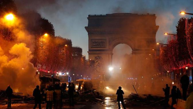 Asap membumbung dekat Arc de Triomphe saat kerusuhan menentang kenaikan harga bahan bakar di Paris, Prancis, Sabtu (24/11). Polisi memasang penghalang logam di sekitar Champs-Élysées untuk menghentikan pergerakan demonstran. (AP Photo/Christophe Ena)