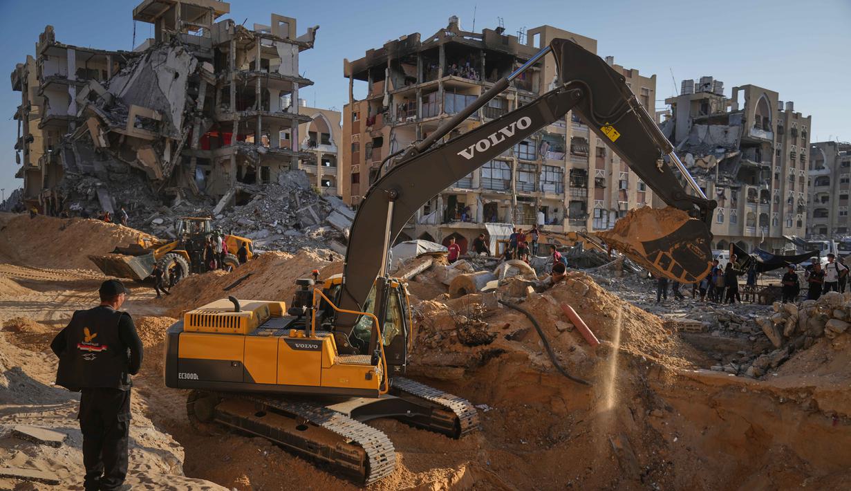 Warga Palestina menyaksikan alat berat dan beberapa pekerja dari Mesir mencari jenazah sandera di Kota Hamad, Khan Younis, bagian selatan Jalur Gaza, pada Minggu 26 Oktober 2025. (AP Photo/Jehad Alshrafi)