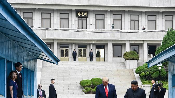 Presiden Amerika Serikat, Donald Trump bersama Pemimpin Korea Utara, Kim Jong-un berjalan menuju garis yang memisahkan kedua wilayah Korea di zona demiliterisasi Korea (DMZ), Desa Panmunjom pada Minggu (30/6/2019).  (Brendan Smialowski/AFP)