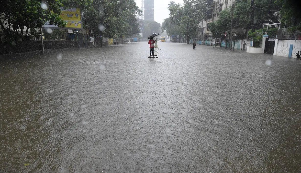 Pria berdiri di pembatas jalan yang tergenang air setelah hujan lebat di Mumbai, India (9/7). Departemen Meteorologi India mengeluarkan peringatan banjir akibat hujan deras di tempat-tempat terpencil di wilayah tersebut. (AFP Photo/Indranil Mukherjee)