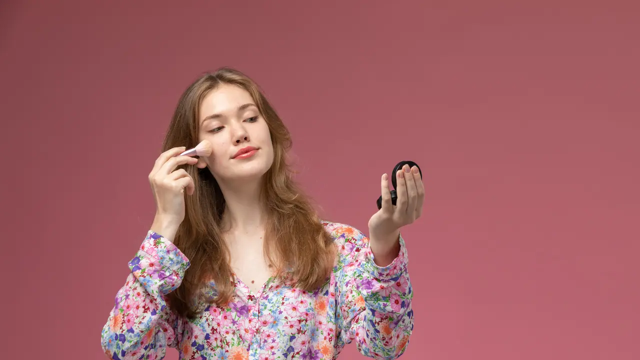 Seorang perempuan sedang mengaplikasikan makeup di bagian pipinya (Foto Dok: Freepik/KamranAydinov)