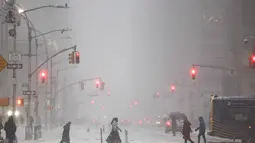 Badai menyebabkan ribuan penerbangan dibatalkan hingga pemadaman listrik besar-besaran. Tampak dalam foto, orang-orang berjalan melintasi Sixth Avenue saat salju turun di distrik Manhattan, Kota New York, pada Minggu 25 Januari 2026. (CHARLY TRIBALLEAU/AFP)
