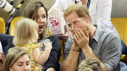 Pangeran Harry bereaksi saat memergoki Emily Henson mengambil popcornnya saat acara Invictus Games 2017 di Toronto, Kanada, Rabu (27/9). Pangeran Harry pun mengganggu bocah itu  dengan memasang wajah isengnya. (CHRIS JACKSON/GETTY IMAGES/AFP)