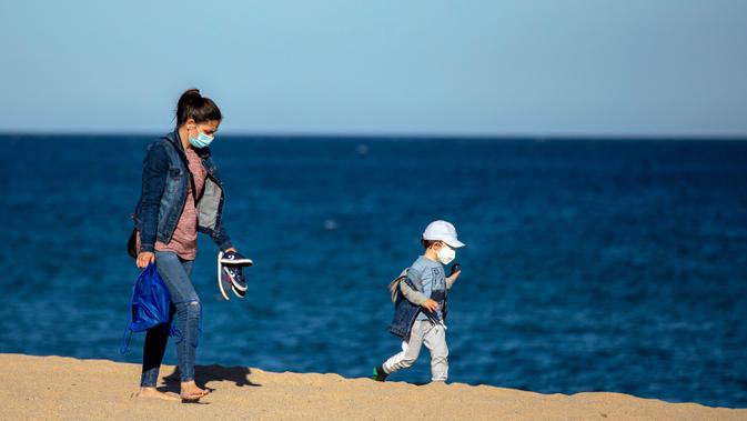 Seorang wanita dan putranya mengenakan masker berjalan menikmati pantai di Badalona, dekat Barcelona, Spanyol, Selasa,(28/4/2020).  Lockdown untuk memerangi penyebaran virus corona terus berlanjut di Spanyol. (AP Photo/Emilio Morenatti)