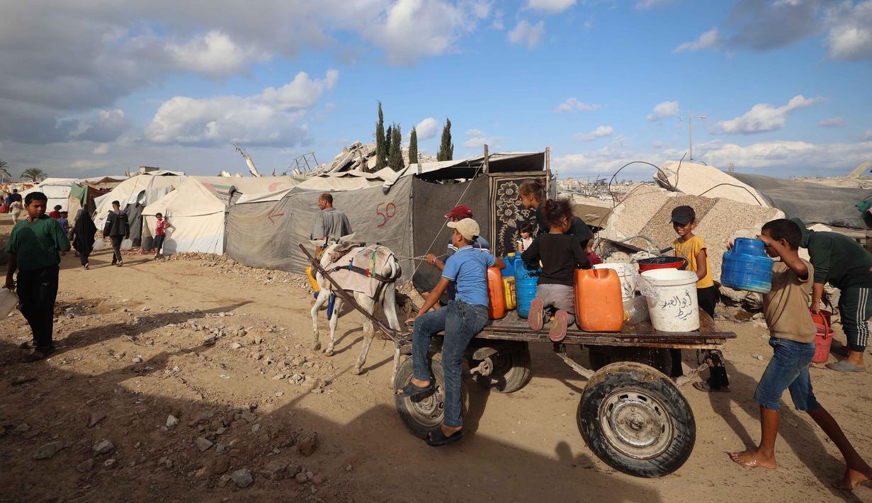 Warga dan anak-anak Palestina mengangkut jeriken berisi air bersih dari tangki air bergerak dengan gerobak keledai di kamp pengungsi Bureij di Jalur Gaza tengah pada 6 Oktober 2025. (Eyad BABA/AFP)