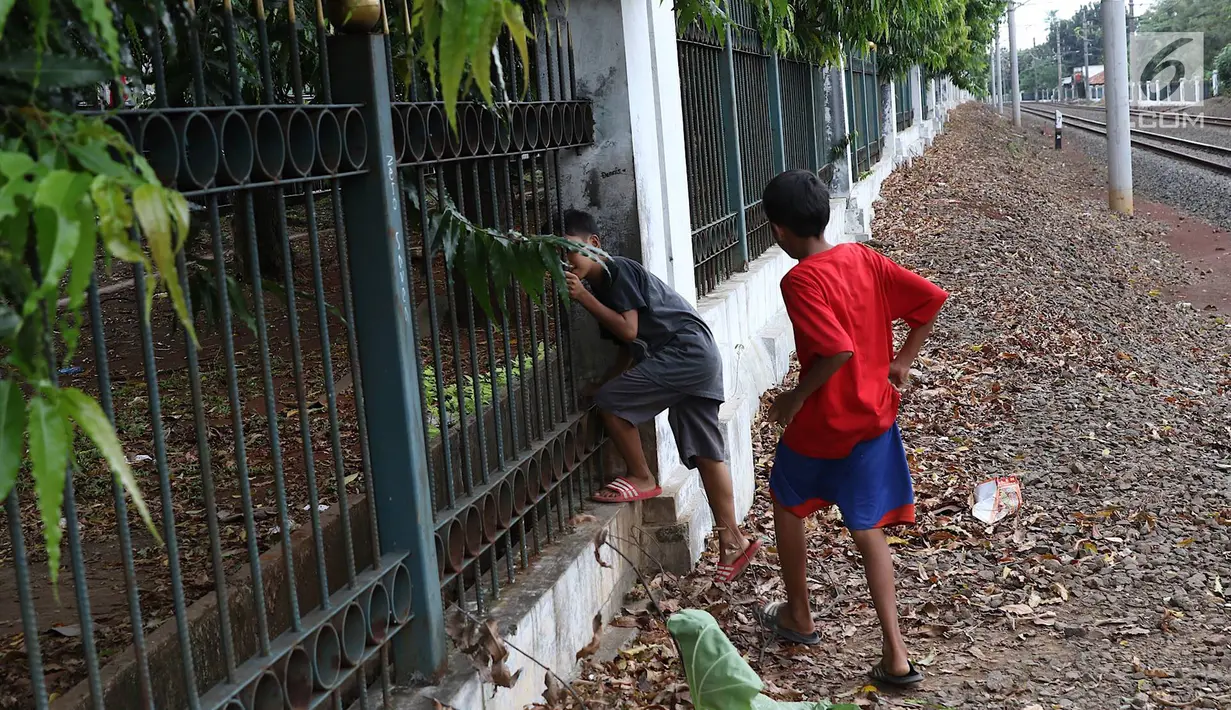 Dua anak menerobos pagar usai menyeberangi rel kereta api di kawasan Lenteng Agung, Jakarta, Selasa (19/3). Tidak adanya JPO menyebabkan warga menerobos pagar besi, meskipun perilaku tersebut berbahaya bagi keselamatan. (Liputan6.com/Immanuel Antonius)