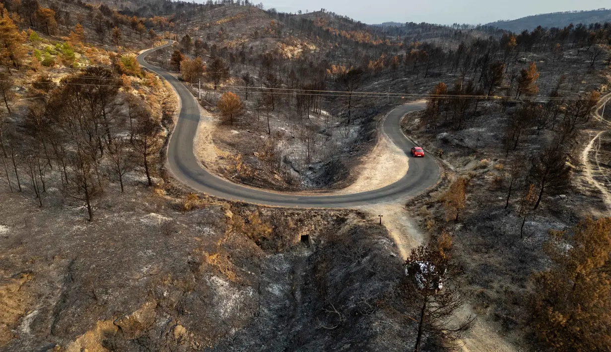 Pemandangan udara ini menunjukkan sebuah jalan yang membentang di sepanjang lahan yang terbakar akibat kebakaran hutan di dekat desa Jonquieres, di departemen Aude, Prancis Selatan, pada 18 Agustus 2025. (Lionel BONAVENTURE/AFP)