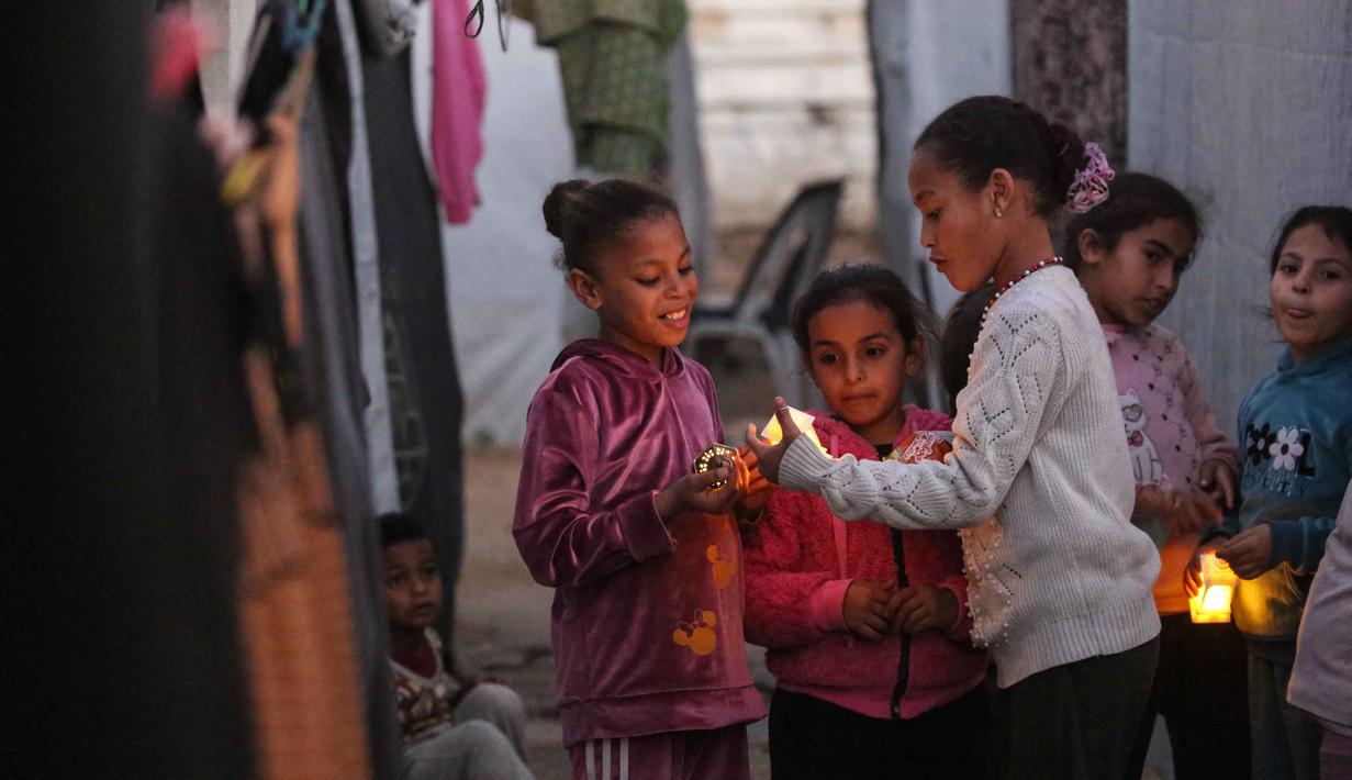 Bagi mereka dan keluarga yang tinggal di lokasi pengungsian, tradisi menyambut Ramadan tetap dijaga sebisanya. Tampak dalam foto, para pengungsi muda Palestina bermain dengan lampion Ramadan saat dekorasi dipasang di samping tenda mereka di kamp pengungsi Bureij di Jalur Gaza tengah pada 15 Februari 2026. (Eyad Baba/AFP)