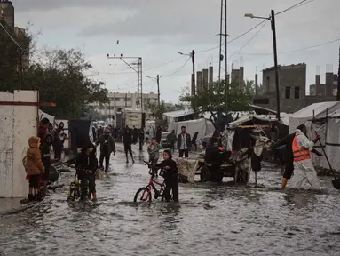 Warga Palestina berjalan di jalanan yang terendam banjir di samping kamp tenda sementara setelah hujan deras di Deir al-Balah, Jalur Gaza tengah, Selasa 25 November 2025. Banjir kembali menggenangi sebagian wilayah Deir al-Balah, Jalur Gaza tengah, pada Selasa 25 November 2025. (AP Photo/Abdel Kareem Hana)