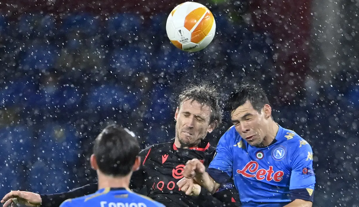Bek Real Sociedad, Nacho Monreal (tengah) dan penyerang Napoli, Hirving Lozano (kanan) melakukan sundulan pada matchday terakhir Grup F Liga Europa di Diego Armando Maradona, Jumat (11/12/2020) dini hari WIB. Napoli bermain imbang 1-1 melawan Real Sociedad. (Alberto PIZZOLI / AFP)