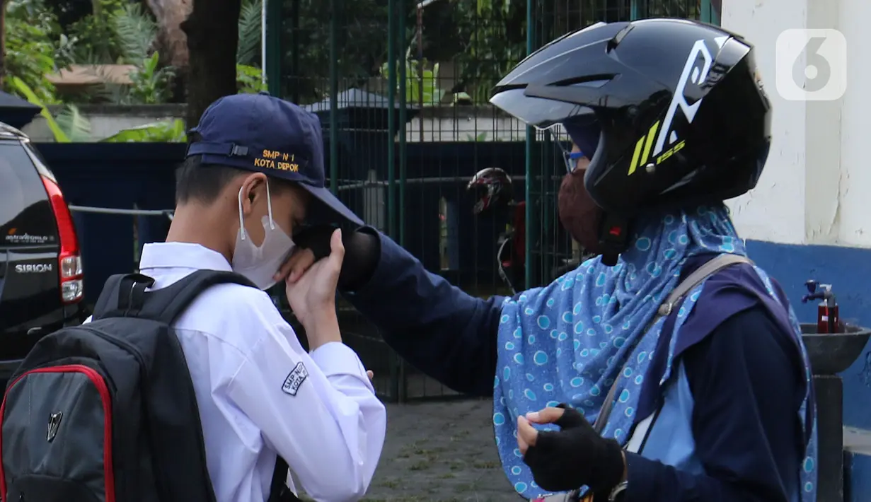 Siswa mencium tangan seorang wanita saat Pembelajaran Tatap Muka Terbatas (PTMT) di SMPN 1 Depok, Depok, Jawa Barat, Senin (4/10/2021). Pemerintah Kota Depok kembali memberlakukan PTMT kepada seluruh sekolah mulai hari ini. (Liputan6.com/Herman Zakharia)