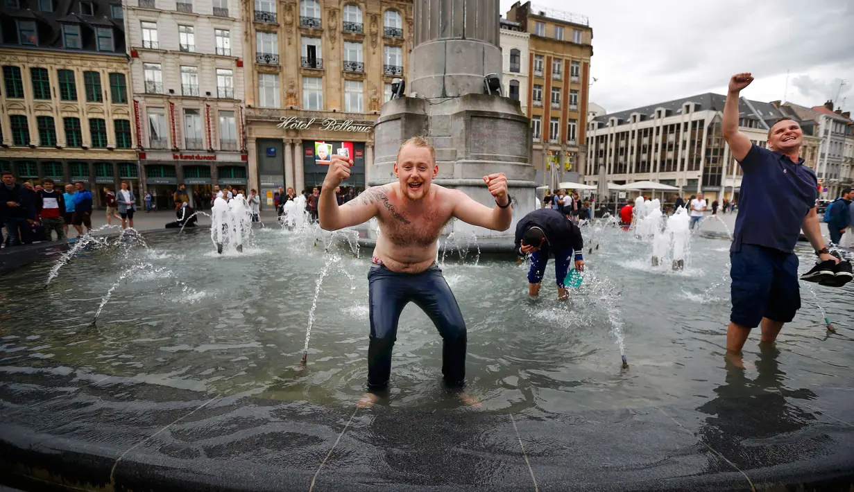 Sejumlah suporter Inggris masuk ke kolam air mancur yang berada di tengah Kota Lille, Prancis (16/6).Aksi suporter Inggris menjadi tontonan warga yang melintasi kawasan tersebut. (REUTERS / Wolfgang Rattay)