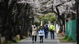 Sejumlah warga berjalan di bawah pohon sakura yang sedang mekar bunganya di distrik Taito, Tokyo, Jepang (26/3). Pohon sakura berbunga setiap satu tahun sekali, kuncup bunga sakura mulai terlihat di akhir musim dingin pada bulan Maret. (AFP Photo/Charly Triballeua)