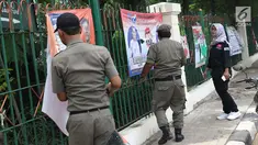 Petugas Satpol PP bersama Panwaslu kecamatan Ciracas menurunkan APK yang terpasang di pagar pembatas antara jalan dengan taman di pinggir kali di sekitar Jalan Raya Bogor, Jakarta, Rabu (23/1). (Liputan6.com/Helmi Fithriansyah)