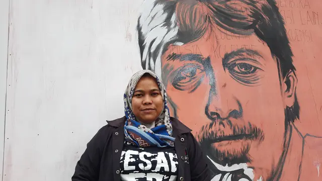 Koordinator KontraS Aceh, Azharul Husna berfoto dengan latar belakang mural wajah Munir Said Thalib (Liputan6.com/Rino Abonita)