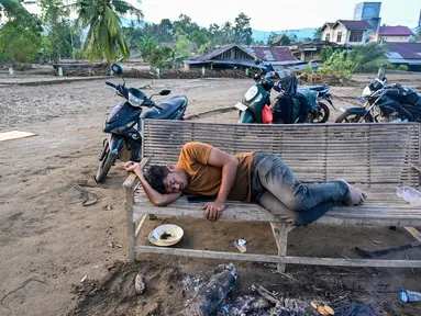 Seorang warga desa yang terdampak banjir tidur di bangku setelah banjir bandang melanda Meureudu, Kabupaten Pidie Jaya, Provinsi Aceh, pada 30 November 2025. Berdasarkan data dari Badan Penanggulangan Bencana Daerah (BPBD) Kabupaten Pidie Jaya, pada Jumat (28/11/2025), jumlah warga terdampak bencana hidrometerologi mencapai 90.000 jiwa dan yang mengungsi sekitar 12.000 jiwa. (CHAIDEER MAHYUDDIN/AFP)