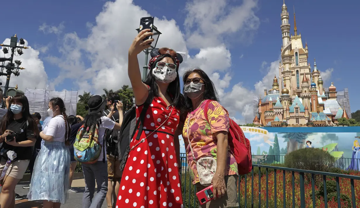 Para pengunjung yang mengenakan masker untuk mencegah penyebaran COVID-19 berswafoto di Disneyland Hong Kong, Kamis (18/6/2020). Disneyland Hong Kong kembali beroperasi pada 18 Juni 2020 dengan menerapkan sejumlah protokol kesehatan baru. (AP Photo/Kin Cheung)