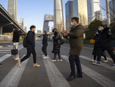 Para komuter yang mengenakan masker untuk melindungi diri dari COVID-19 menyeberang jalan di Beijing, China, Rabu (15/12/2021). China mendeteksi kasus kedua varian omicron pada seorang pria berusia 67 tahun yang dinyatakan positif setelah lebih dari dua minggu karantina. (AP Photo/Mark Schiefelbein)