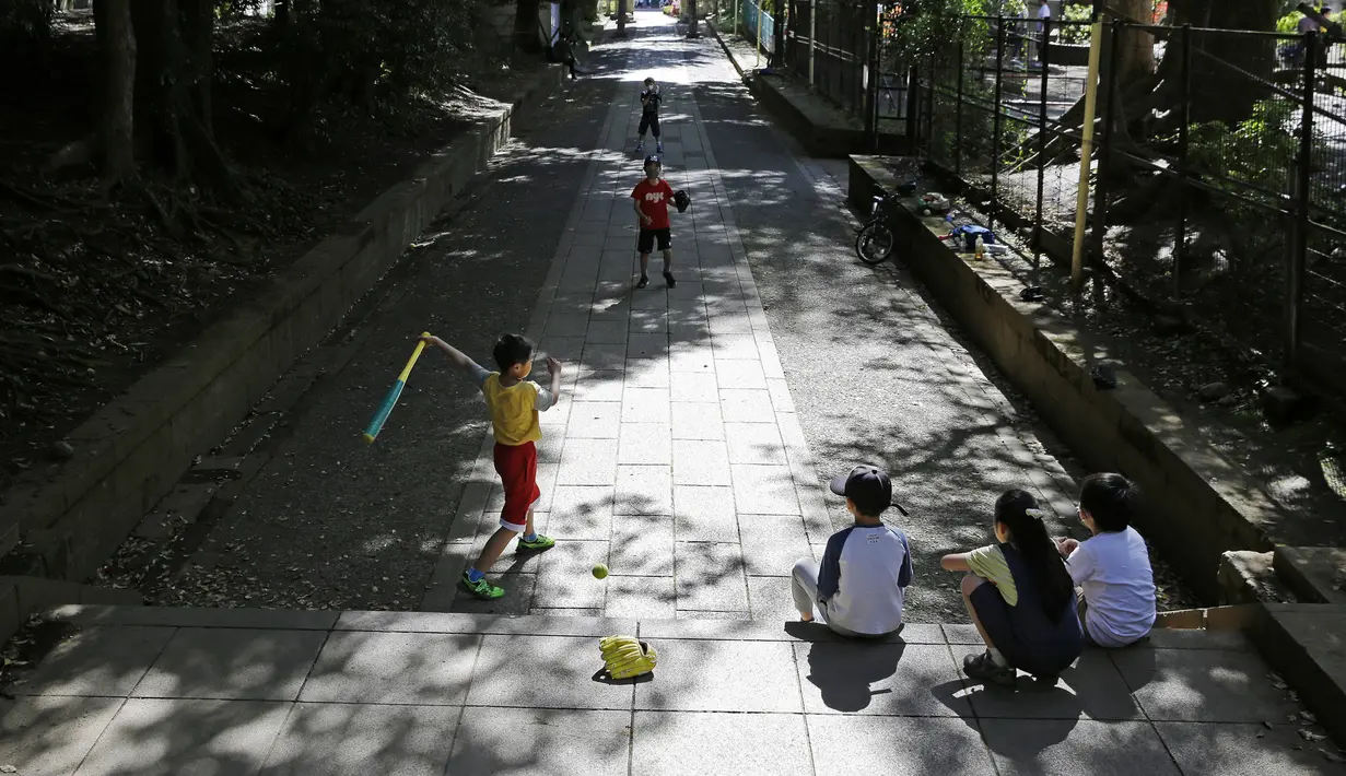 Anak-anak bermain bisbol di jalan setapak menuju kuil Shinto Hikawa-Jijja shinto, Tokyo, Jepang, 19 April 2020. Daya tarik liburan menguji persatuan masyarakat dalam menghadapi virus corona COVID-19. (AP Photo/Kiichiro Sato, File)