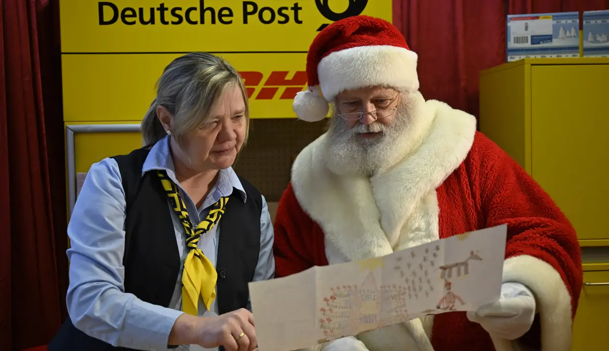 Seorang pria berkostum Sinterklas dan karyawan dari layanan pos Jerman, Deutsche Post membaca daftar keinginan seorang anak di Kantor Pos Natal di Himmelpfort, Jerman pada 19 Desember 2018. (Tobias SCHWARZ/AFP)