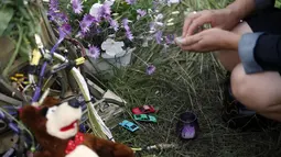 Salah satu warga meletakkan untaian bunga dan mainan anak di dekat lokasi jatuhnya pesawat Malaysia Airlines MH-17 di Donetsk, Ukraina, (19/7/2014). (REUTERS/Maxim Zmeyev)