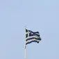 Seorang pendukung mengangkat tangan tanda kemenangan disamping bendera Yunani atas parlemen di Athena, Yunani (6/7/2015).  Parlemen Eropa Heald sidang paripurna pada tanggal 7 Juli pada konsekuensi dari hasil referendum Yunani.  (REUTERS/Yannis Behrakis)