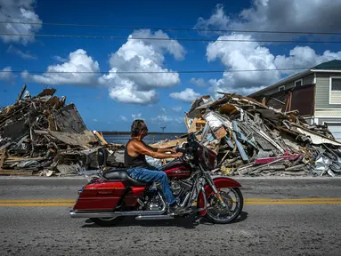 Seorang pengendara sepeda motor melewati puing-puing yang menumpuk dari rumah yang hancur setelah melewati Badai Ian di Pulau Matlacha di Lee County, Florida pada 7 November 2022. Pantai timur Florida berada di bawah pengawasan badai saat negara bagian itu bergulat dengan kehancuran Badai Ian. (AFP/ Giorgio Viera)