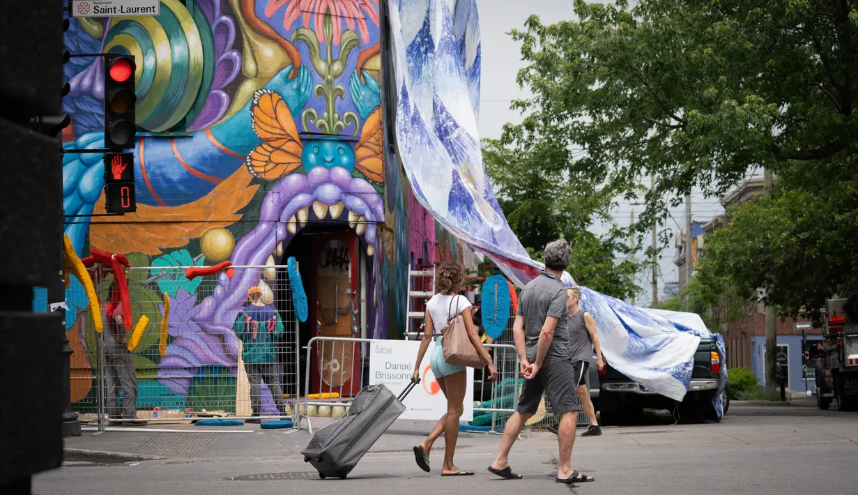 Orang-orang menonton seniman bekerja saat Festival Mural Montreal di Quebec, Kanada, 16 Juni 2022. Dimulai pada tahun 2012, acara seni jalanan itu ingin dinobatkan sebagai "pemimpin seni urban" di Amerika Utara, kata penyelenggara Pierre-Alain Benoit kepada AFP. (Paola Chapdelaine/AFP)