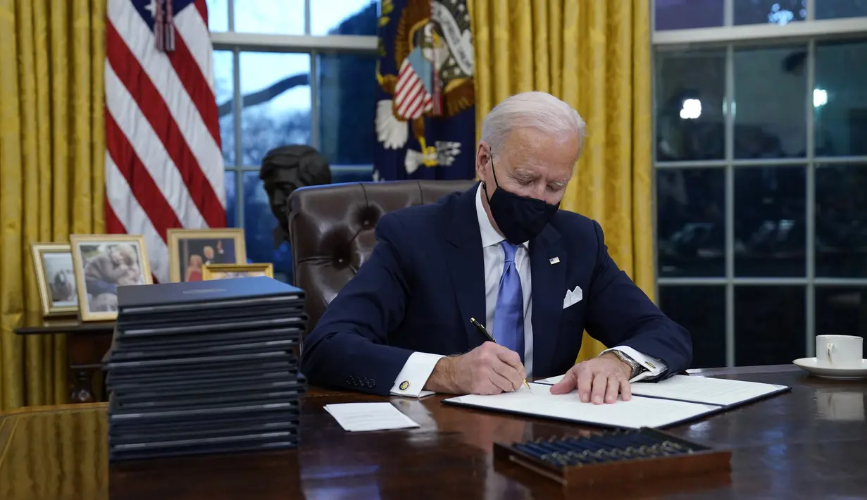 Presiden Joe Biden menandatangani perintah eksekutif pertamanya di Ruang Oval, Gedung Putih di Washington, Rabu (20/1/2021). Pada hari pertamanya menjabat, Presiden Amerika Serikat Joe Biden menandatangani sejumlah tindakan eksekutif di Gedung Putih. (AP Photo/Evan Vucci)