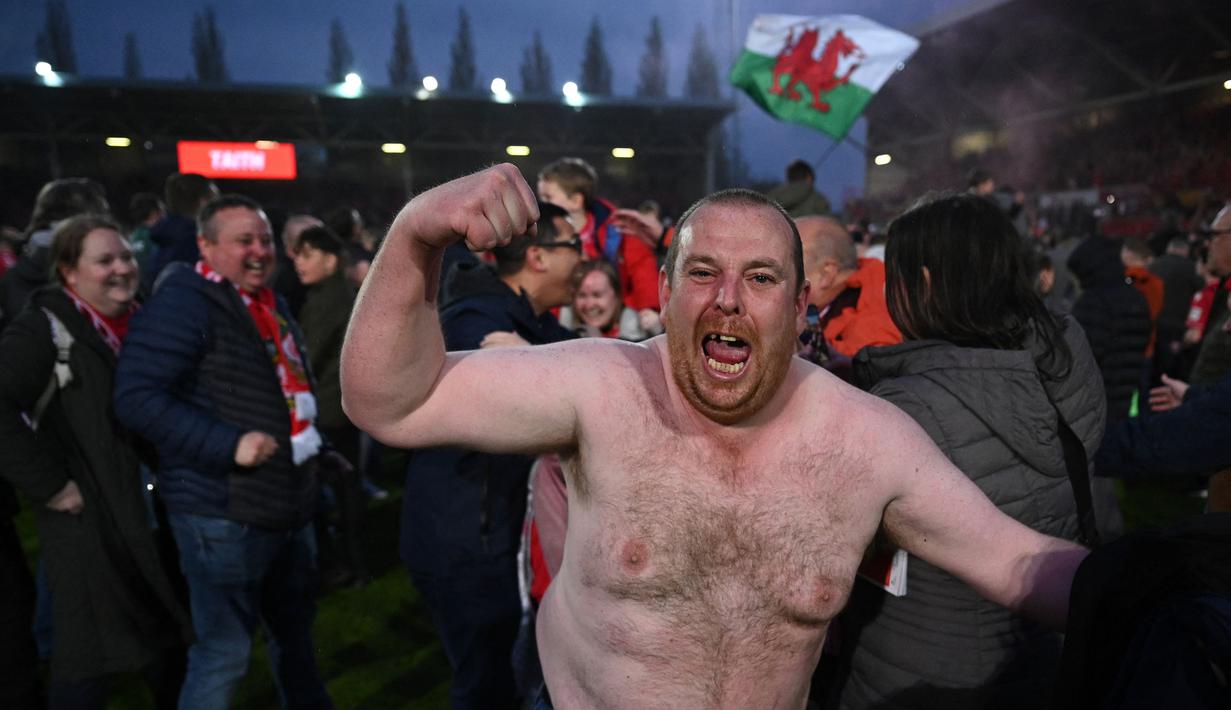 Pendukung Wrexham merayakan kemenangan timnya saat laga English National League antara Wrexham melawan Boreham Wood di Racecourse Ground Stadium, Wrexham, Wales, Sabtu (22/04/2023). Wrexham menang dengan skor 3-1 dan berhasil promosi ke Liga Dua Inggris. (AFP/Oli Scarff)